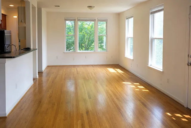 An empty living room with wood floors and three windows