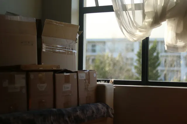 Taped moving boxes stacked by a window with a sheer curtain